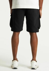 Pantaloni cargo neri con tasche laterali, realizzati in tessuto testurizzato, con un taglio dritto e una vita liscia. Indossati con sneaker bianche.