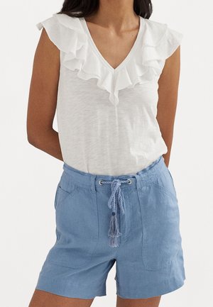 Femme portant un haut blanc sans manches à volants et un short taille haute bleu clair avec une ceinture tressée à nouer et des poches à l'avant.