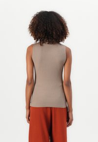 Sleeveless, ribbed brown top featuring a fitted design and crew neck. Worn with loose, rust-colored pants; smooth fabric texture.