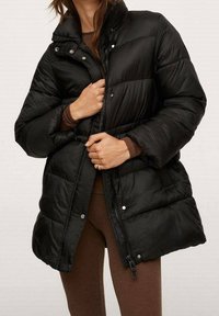 Giubbotto piumino nero con colletto alto, bottoni a pressione e chiusura con zip. Presenta sezioni trapuntate e tasche laterali, realizzato in un materiale lucido e liscio.