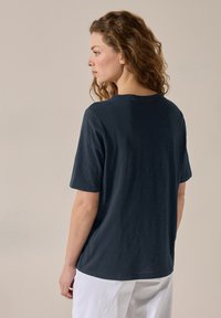 Námořnická modrá, krátký rukáv, tričko s kulatým výstřihem, volný střih, měkká textura a spadlými ramenními švy. Nosené s bílými kalhotami.