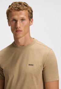 Beige Rundhalsausschnitt-T-Shirt aus weichem Stoff, mit kurzen Ärmeln und einem kleinen schwarzen "BOSS"-Logo auf der Brust. Angenehme Textur.