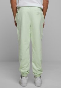 Pantalones de chándal verde claro hechos de una tela suave, que cuentan con un bolsillo trasero y puños elásticos en los tobillos. Combinados con zapatillas blancas.