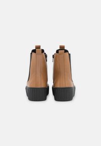 Brown leather ankle boots with black elastic sides and a textured black sole. Features include a rear zipper and pull tab for easy wear.