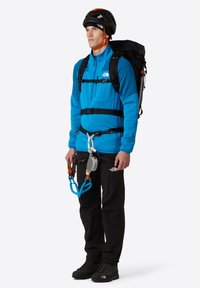 Giacca di pile blu, pantaloni neri e attrezzatura da arrampicata. Include un casco, uno zaino, un'imbracatura e moschettoni. Design testurizzato e funzionale.