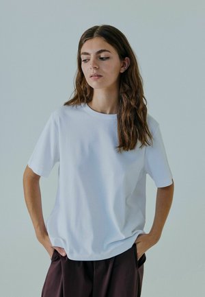Witte katoenen T-shirt met een ronde hals en korte mouwen, met een relaxte pasvorm en een gladde textuur, gedragen met donkerbruine broek.