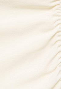 Tela de color crema con una textura suave y un ligero brillo, que presenta secciones fruncidas a lo largo de un borde para un detalle adicional.