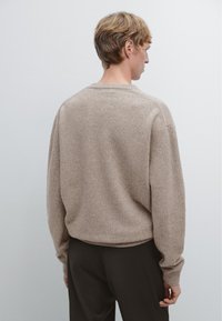 Ljust brunt, texturerat tröja med avslappnad passform, sänkt axlar och ribbade ärmslut. Designad med en vid halsringning och en kort längd.