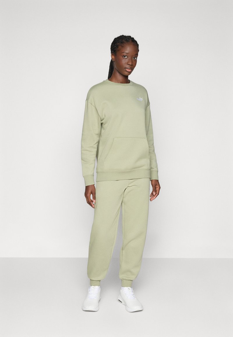 Felpa verde chiaro e pantaloni coordinati realizzati in tessuto morbido, con una tasca frontale e un piccolo logo sul petto. Sneakers bianche.
