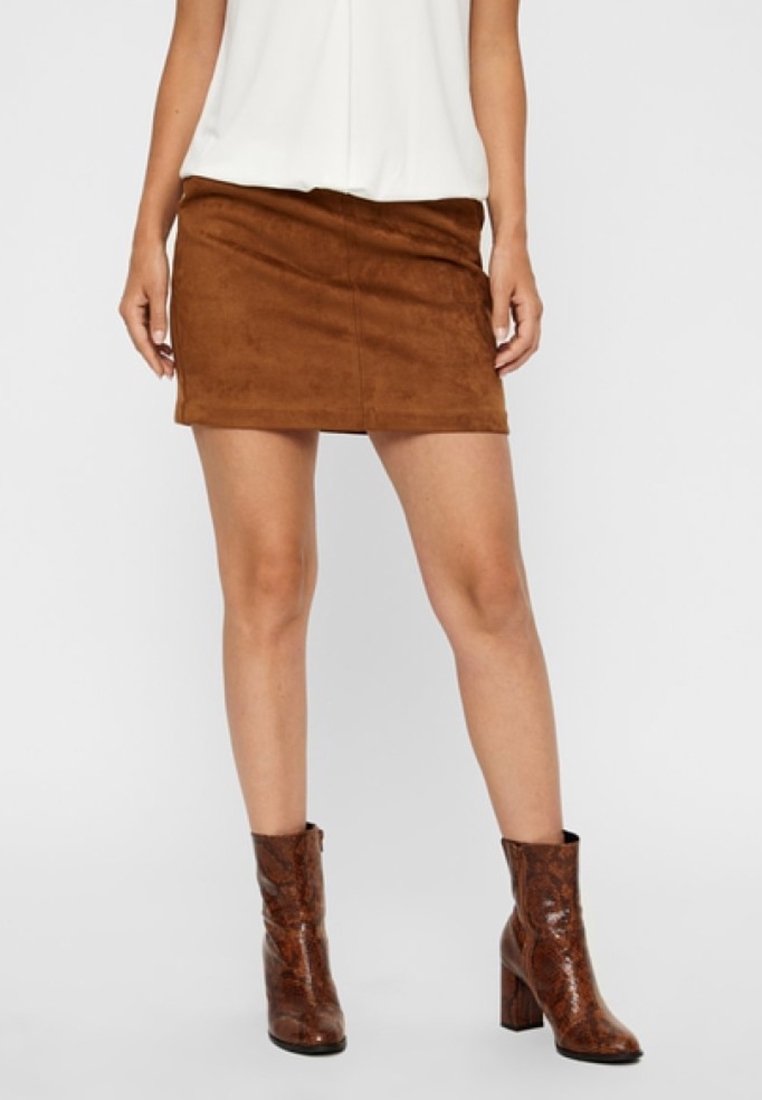 Femme portant un débardeur blanc, une mini-jupe en daim marron et des bottines marron texturées à talons carrés.