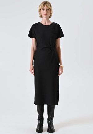 Abito nero midi con maniche corte, realizzato in un tessuto morbido. Presenta un sottile dettaglio a torsione in vita. Abbinato a stivali neri al ginocchio.