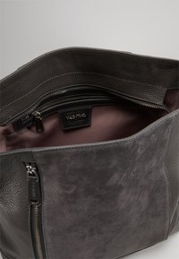 Szara skórzana torba z teksturowaną powierzchnią, zamszowymi akcentami, dwoma zamykanymi na zamek komorami oraz gładkim wyściełaniem wnętrza. W środku widoczna metka marki.