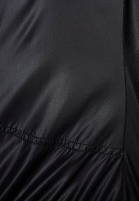Tessuto di raso nero con una texture liscia, caratterizzato da cuciture arricciate lungo l'orlo e una leggera lucentezza. Design semplice senza motivi.