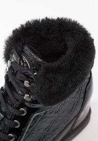 Czarne zimowe botki typu high-top z teksturowanym boku, metalowymi oczkami, grubymi czarnymi sznurówkami i miękkim, puszystym wykończeniem kołnierza.