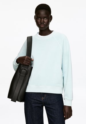 Light blue sweatshirt with a crew neckline and ribbed cuffs, paired with dark blue jeans. Black leather bag with adjustable strap.