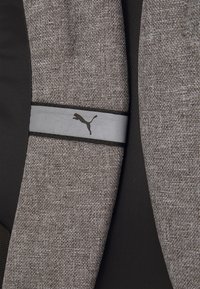 Puma bunda s texturovanou šedou tkaninou a černými akcenty. Výrazný šedý pásek zobrazuje logo Puma a hladký povrch.