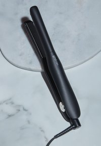 Mini lisseur de cheveux ghd noir avec cordon pivotant reposant sur une surface en marbre blanc.