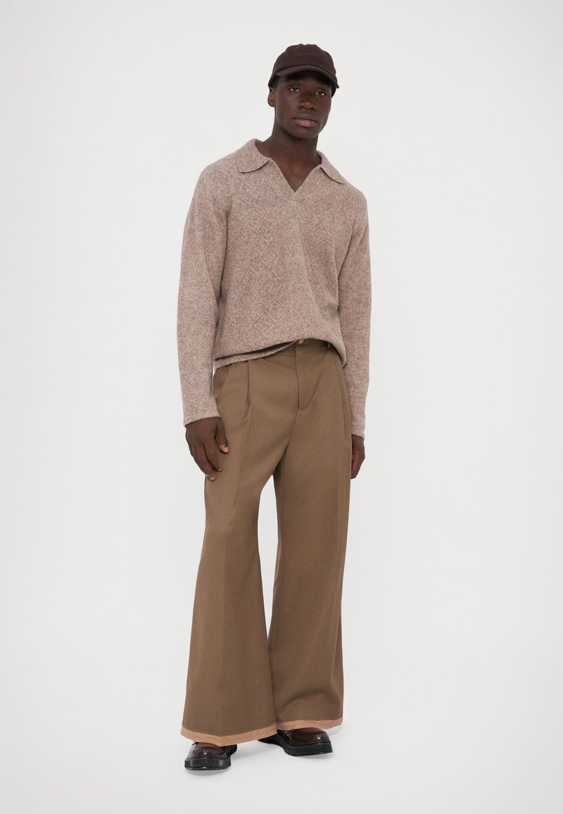 Pull en laine texturé de couleur marron clair avec un large col, associé à un pantalon marron taille haute et ample, et des chaussures sombres à enfiler.