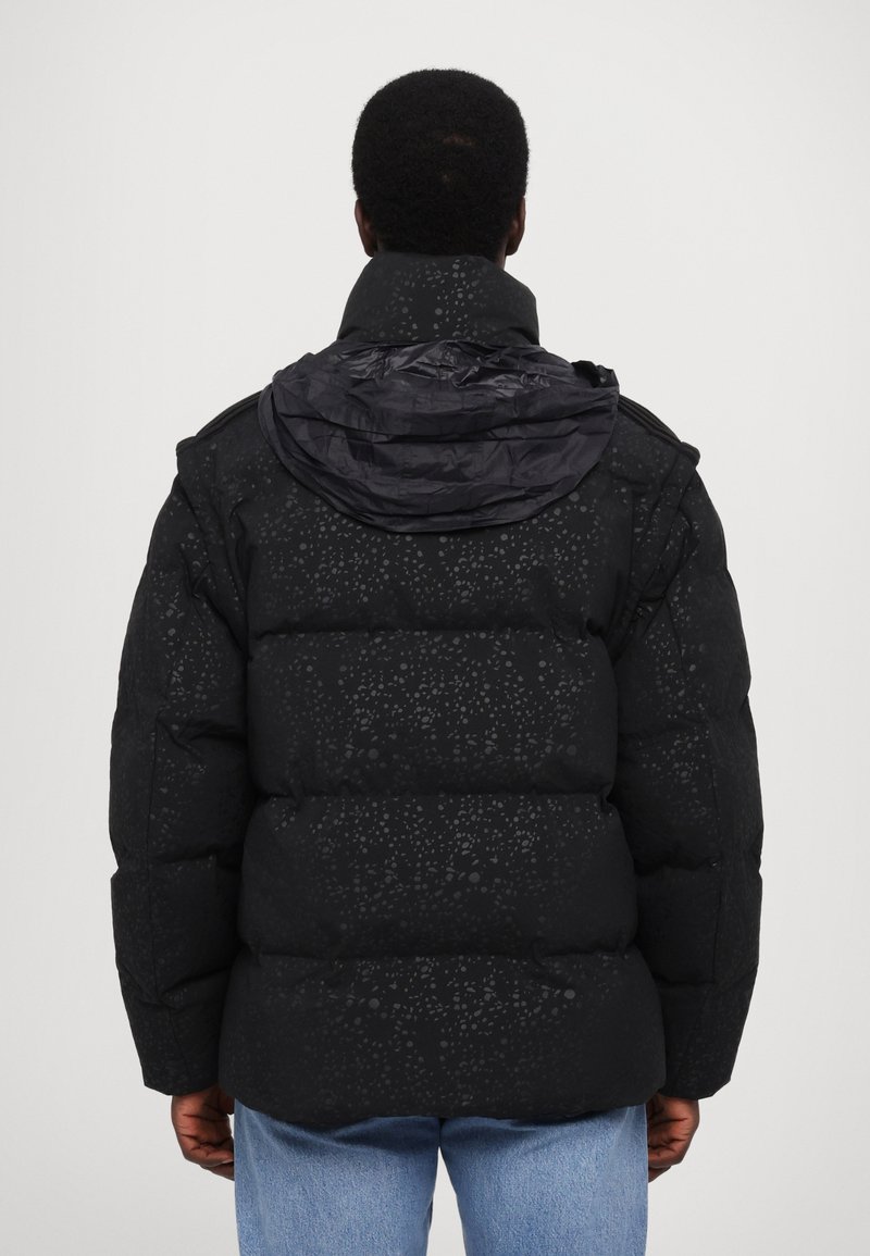 Czarna kurtka puchowa o teksturowanym wzorze, z dużym kołnierzem i wyraźnym kapturem. Posiada prostokątny kształt i grubą izolację.