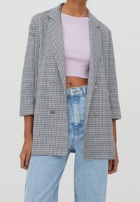 Black and white checked blazer with a loose fit, notched lapels, and double-breasted buttons, paired with a light purple top and high-waisted jeans.