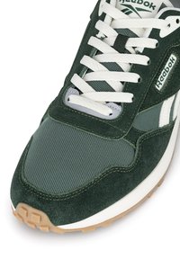 Green suede and mesh sneaker with white laces, Reebok logo, and rubber outsole. Features contrasting textures and a cushioned tongue.