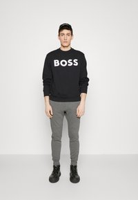 Sudadera negra con gran texto blanco "BOSS", pantalones de chándal ajustados grises y botas negras de cordones. Ropa atlética sencilla y casual.