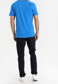 Blå bomullst-shirt med korta ärmar, rygglogo, kombinerad med mörka jeans och vita sneakers, som visar en avslappnad outfit.