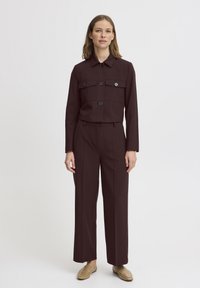Burgundy two-piece outfit featuring a collared jacket with buttons and two front pockets, paired with wide-leg trousers. Smooth texture throughout.
