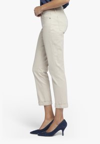 Beige bavlněné kalhoty se rovnými nohavicemi, ohrnutými lemy a pasem s poutky na opasek. Nosené s vysokými podpatky v námořnické modré z semiše.