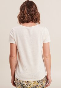 T-shirt a maniche corte di colore crema in un tessuto morbido e leggero, con scollatura a girocollo e orlo leggermente curvato.