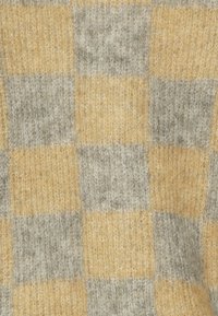 Tessuto a maglia in un motivo a scacchi con quadrati alternati di giallo pallido e grigio chiaro. La trama appare morbida e accogliente.