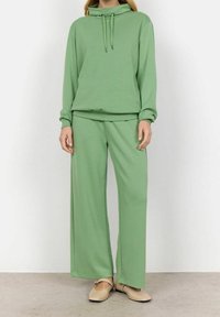 Sudadera con capucha verde y pantalones de pierna ancha hechos de material suave y ligero. Presenta un cordón ajustable y un corte relajado.