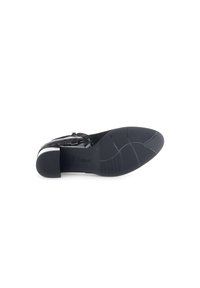Zwarte lakleren schoen met een lage hak, voorzien van een spitse neus en textuurdetails op het oppervlak. Soepele buitenzool met grippatroon.