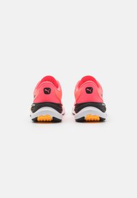 Zapatillas deportivas rosas con parte superior de tela texturizada, media suela negra y suela amarilla; presenta un acento de logo en el talón y el costado.