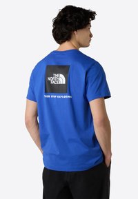 Blå bomulds t-shirt med rund hals. Har et sort firkantet grafisk motiv med "THE NORTH FACE" og "NEVER STOP EXPLORING" på ryggen.