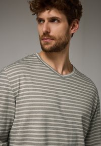 Světle šedé tričko s výstřihem do V, úzkými černými pruhy, krátkými rukávy a volným střihem. Bavlněný materiál se soft texturou.