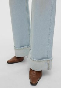 Šviesiai mėlynos plačios kojos džinsai su sukamuoju apdailu, derinami su smailiu antblauzdžiu iš rudos odos. Akcentuojamas tekstūros ir elegantiško dizaino derinys.