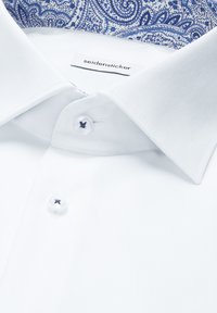 Chemise blanche avec un col structuré, présentant un motif paisley bleu à l'intérieur. Comprend des boutons blancs avec des accents de couture bleu marine.