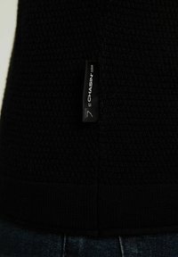 Svart stickad tröja med ett texturerat mönster, med en märkesetikett på sidan och en ribbad fåll.