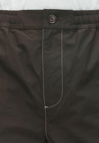 Pantalons noirs avec une taille élastique, fermeture à bouton et coutures blanches contrastantes sur le détail de la poche avant. Texture de tissu lisse.