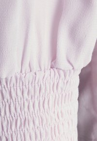 Tecido rosa claro com uma superfície texturizada e detalhes elásticos franzidos. A visão em close destaca o franzido e a textura suave.