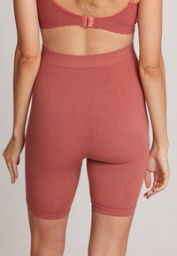 Geribbelde, hoge taille shorts in een terracotta kleur. Heeft een gladde tailleband en knielange pijpen met een subtiele textuur.