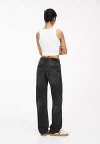 Zwarte denim wijde pijpen jeans met subtiele vervaging, vijf zakken en een klassieke tailleband, gecombineerd met een wit cropped tanktop.