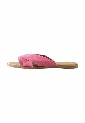 Sandales en suède rose à semelle plate tan, avec des brides croisées et un design minimaliste.