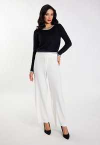 Pulover negru cu margini gri, asortat cu pantaloni albi largi. Modelul poartă tocuri negre ascuțite, pozând pe un fundal neutru.