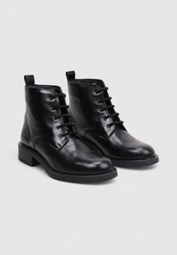 Bottines en cuir noir avec une finition lisse, fermeture à lacets, bout rond et petit talon carré. Comprend une languette pour un enfilage facile.