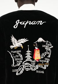 Casaco de veludo preto com um bordado intricado do Japão, que retrata uma águia, uma pagode e uma figura vestida com um quimono, juntamente com os nomes de cidades.