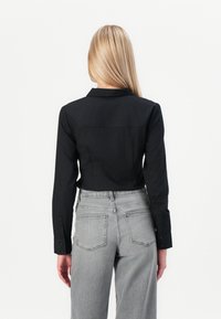 Camicetta nera corta con colletto, maniche lunghe e polsini con bottoni, abbinata a pantaloni in denim grigio a vita alta con tasche applicate.
