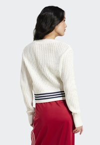 Sweater branco de malha com uma bainha listrada em azul marinho com efeito canelado. Apresenta uma textura de trama solta, mangas longas e decote arredondado.