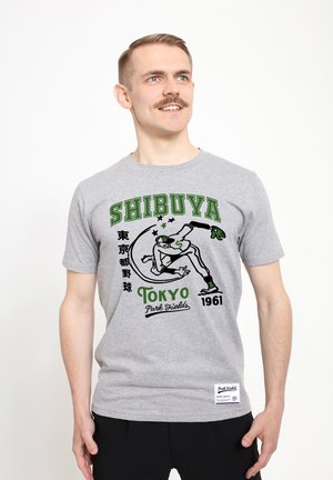 Šedé tričko s zeleným grafickým potiskem skateboardisty, textem "SHIBUYA" a "Tokijské parkové pole 1961", s měkkou bavlněnou texturou.